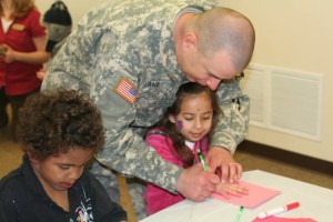 Military man helping little girl trace her hand on paper